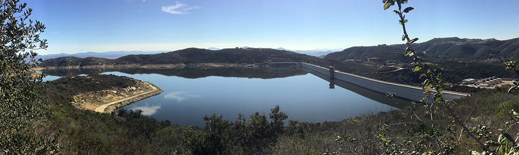 Wide angle view of the reservoir and the long, narrow dam surrounded by dark hilltops.