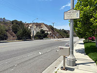 Chino Fault crosses Palisades Avenue at Wardlow Wash. The stream channel follows the fault line. Small sign is historic marker for Highway 18 and US Highway 91. 