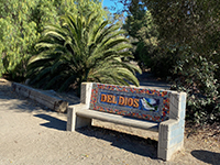 Bench with Del Dios sign next to parking area near Hernandex Hideaway on Lake Drive.