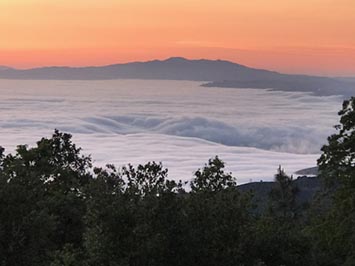 View looking down at a marine layer stratus cloud over Monterey Bay area with Loma Prieta Peak in the Santa Cruz Mountains in the distance.