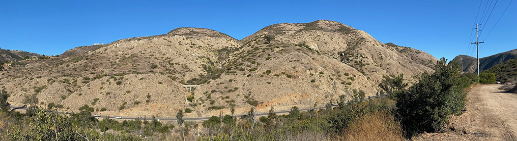 Wide angle view of the Del Dios Gorge, Del Dios Highway, and a mountainside with a large granite sill running across near the top of the slopes.