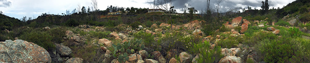 A panoramic view of a large field of boulders and outcrop of orange and white colored rocks of the San Dieguito River floodplain.