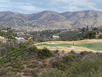 Hilltop view looking over a golf course next to the forested Santa Fe Valley with a brown mountain ridgeline in the distance.