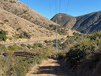 View looking down a trail to a bridge over the stream with the Del Dios Gorge in the distance.