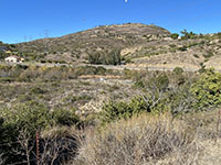 View of the rocky and shrub-covered floodplain with a hillside in the distance.