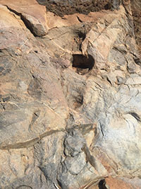 A rocky outcrop with a serices of 4 rounded mortar holes in the rocks along a stream bed.