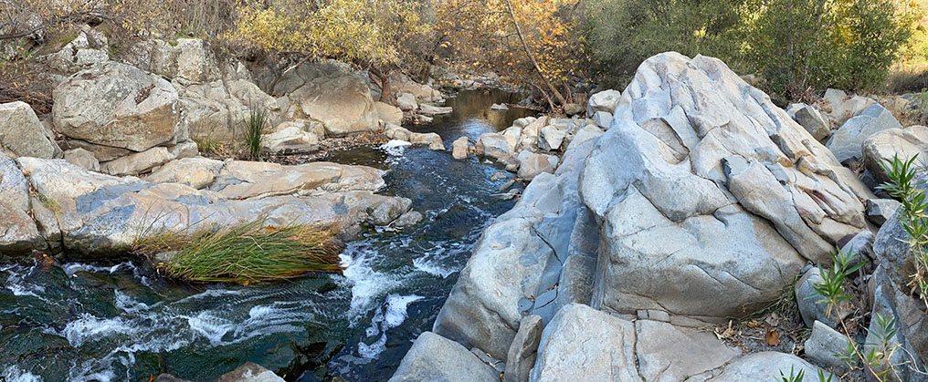 Large gray rocky outcrops and boulders along Escondido Creek with some small rapids.