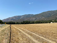 View of a dry grassy field with a dark mountain front in the distance. View looking south from the CA 79 pass pull off toward the fault trace crossing the mountain front along Palomar Mountain and Eagle Crage Mountain.