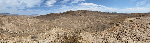 Panoramic view of a brown and barren desert mountain landscape. The view shows the Coyote Mountains with Canyon Sin Nombre to the north (left) and Montero Wash to the south (right). This view is from an unnamed Coyote Mountains overlook area on an unpaved road about a mile south of the Carrizo Badlands Overlook area. The Elsinore Fault runs basically along the base of the south-facing mountain front.
