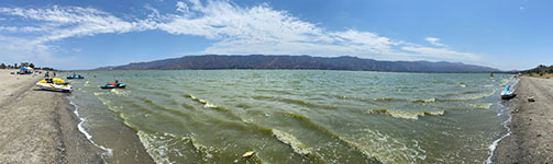 Panoramic view looking south to west across Lake Elsinore from the shoreline shoreline on Lakeview Drive. The Santa Ana Mountains are in the distance. The beach show here roughly follows the Wildomar Fault.