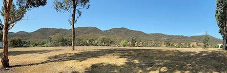This view shows a broad open field with chaparral-covered mountains in the distance. The view shows the mountain front along the eastern side of the Santa Rosa Plateau from Business Park Drive. The Willard Fault splits into parallel and interconnected fault strands along the mountain front west of Temecula, CA.