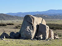 A large free-standing granite bouled wish other boulders in the grasslands.
