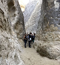View of students hiking and waving while hiking up Annie's Canyon that cuts through the Torrey Sandstone.
