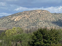 View of the boulder and outcrop-covered mountainside and peak of Raptor Ridge beyond a forest in the foreground.