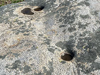 Two small round grinding mortar holes on the lichen-stained surface of a granite outcrop.