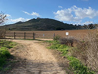 Agricultural fields and low hills beyond a gate at a bend in the Mule Hill Trail.