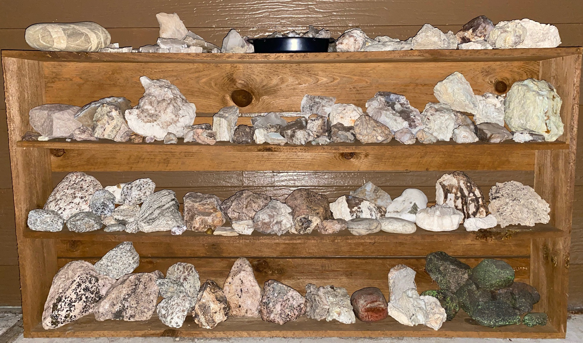 4 shelves of mostly white to light-colored rocks under white xenon flash light (same as shown in fluorecent mineral images).