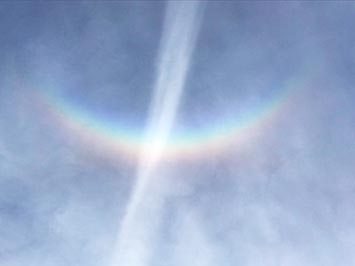 Zoomed in view of a rainbow circumzenithal arc in thin cirrus cloud cover (sun direction at bottom). This arc was directly straight-up overhead, the Sun was at about 45 degrees to the southwest. A contrail crosses the arc.