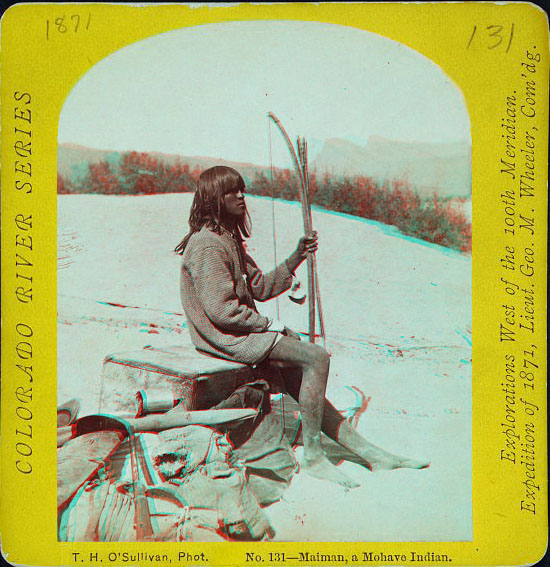 Man sitting with bow and arrow on travel gear on a sand dune