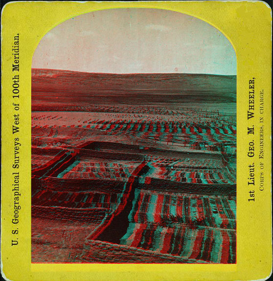 Distant view showing crop fields surround by some low stone walls.