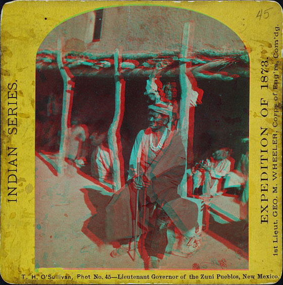 Man sitting next to an adobe building with other people resting in the shade of an overhang.