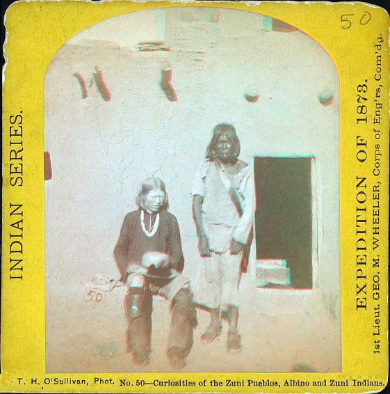 Two indians in front of an adobe home. One is an albino.