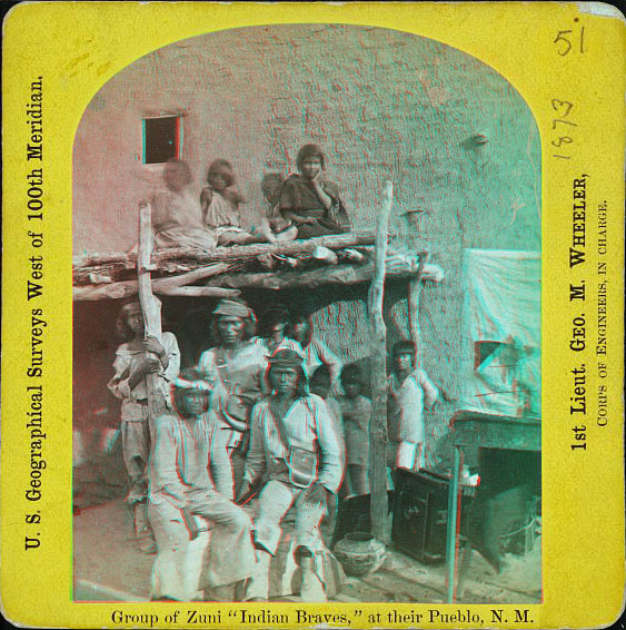 A dozen young people standing and sitting in front of an adobe building. Some are on the roof of a pateo overhang.