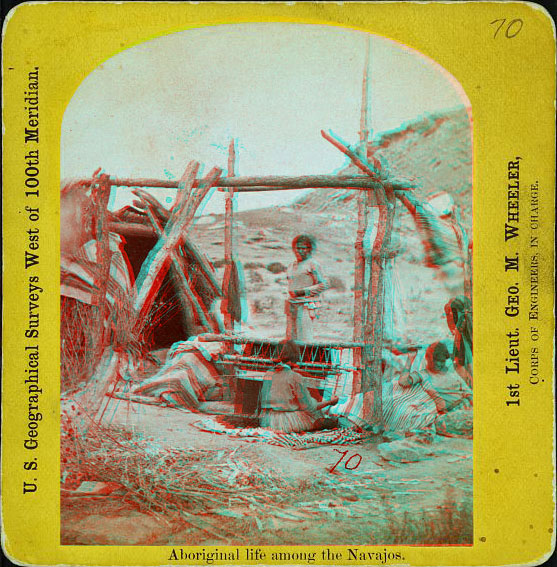 Three women near a weaving setup and a low wooden building nearby.