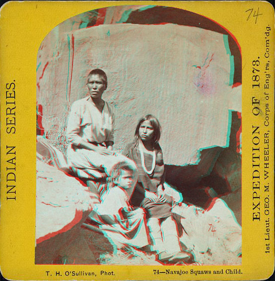 Two women and a child, all in native dress, in front of a large rock