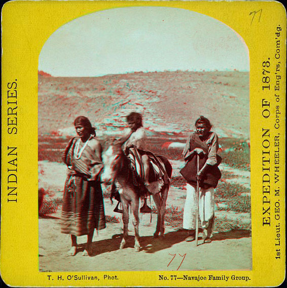 Old woman with a cane, a child on a burrow, and a barefoot woman, all in Native dress, outside with a hill in the distance