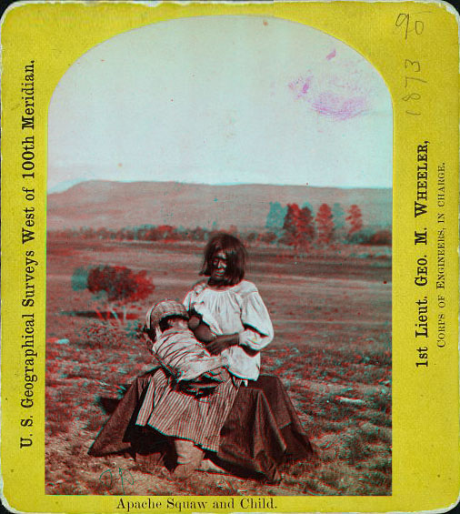 A woman sitting outside, in native dress breast feeding a baby.