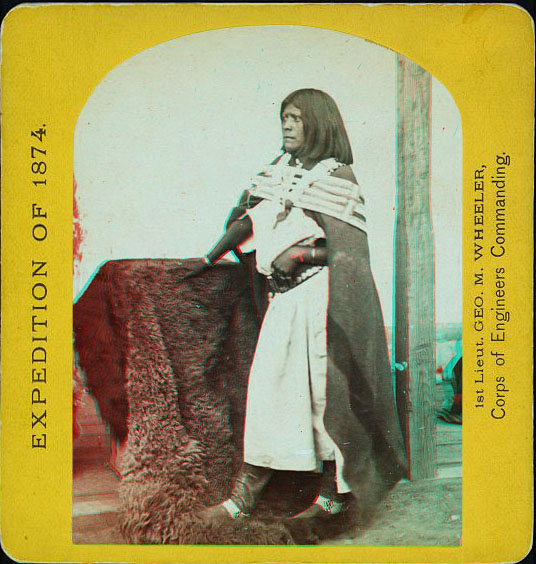 A woman posed in native dress with her hand on a buffalo skin.