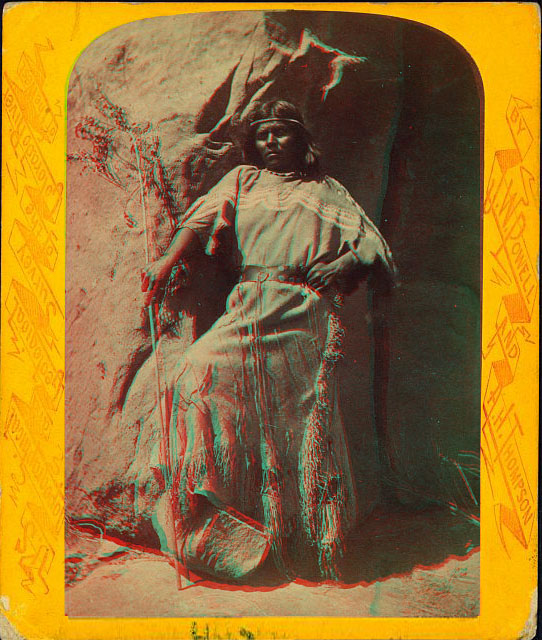 A woman in native dress standing, leaning on a rock