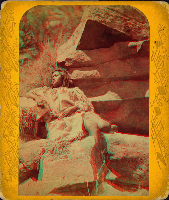 A woman in native dress reclining against some rocks