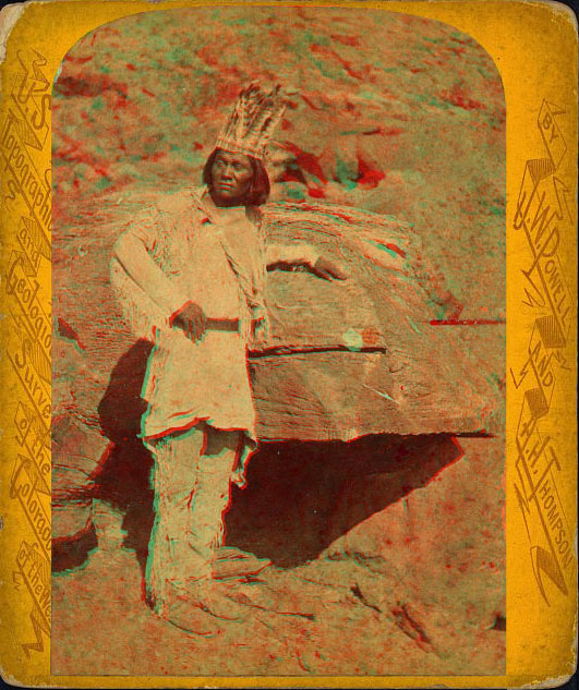 A man in native dress with a feather crown, leaning on a rock