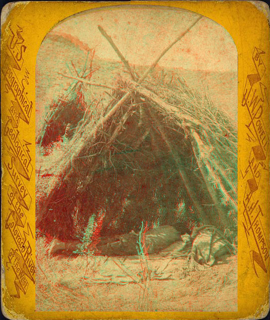 A person laying in the shade of a hut made of sticks