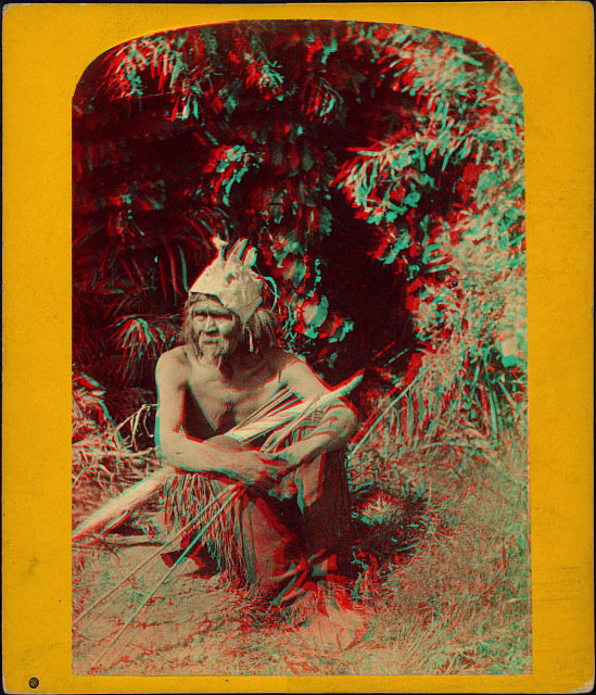 A man sitting holding a bow and arrow, and wearing an unusual headdress