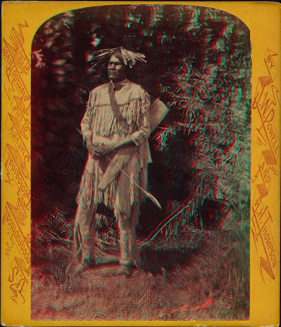 A man in tative dress standing and holding a bow and arrow