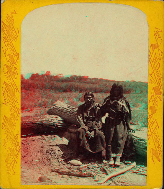 A man and woman in native dess sitting next to some logs