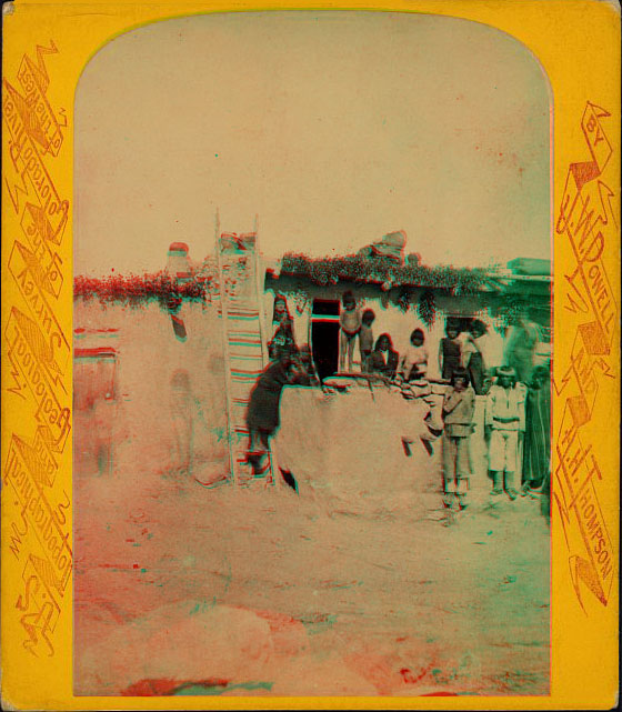 A group of people sitting or standing in front of an adobe building