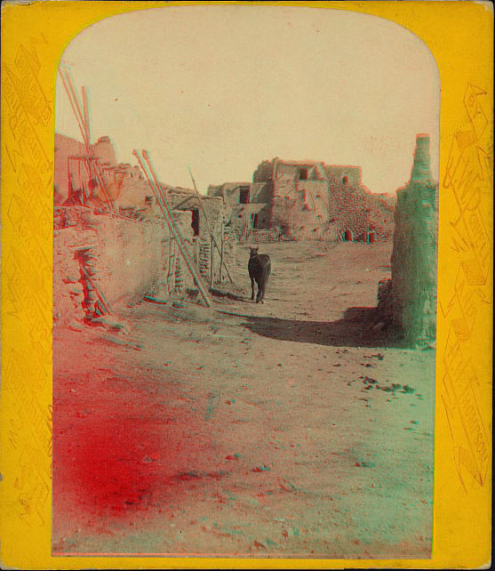 View of a path between rock and adobe buildings with a horse in the view