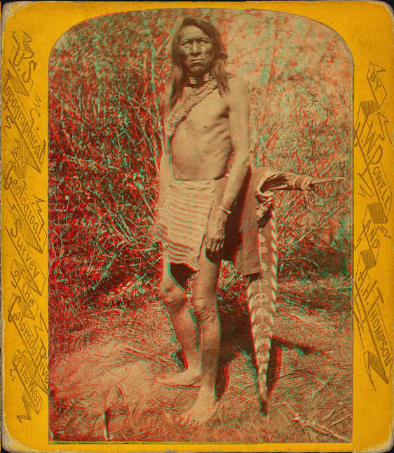 A bare-chested man standing barefoot with a decorated quiver with arrows.