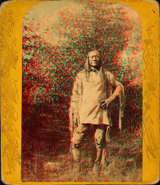 A man in native dress standing outside amid brush