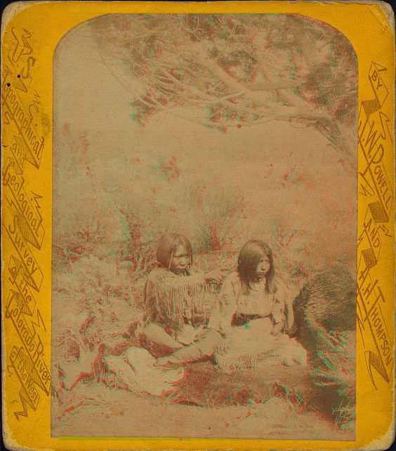 Two youths sitting on a fur blanket. One is pointing