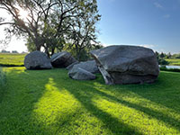 Three large boulders of granite (glacial erratics) in a grassy lawn area next to the quarry lake in Pipestone National Monument.