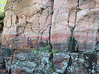 View of the colorful (reds, yellows, and grays) of the cross-bedded Souix Quartzite. Green lichens grow on the lower part of the outcrop.