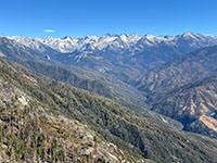 View from Moro Rock of the high show covered peaks and rocky ridgeline of the crest of the Sierra nevada beyond a deep, frested canyon.