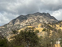 View of a relatively barren mountain peak of gray granite with grasslands and oak forest in th foreground.